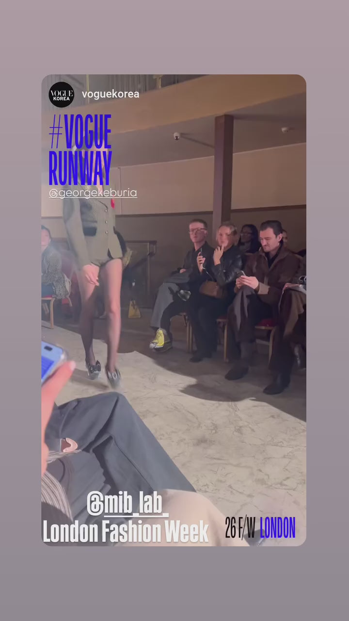 Défilé London Fashion Week : plusieurs mannequins défilent sur le runway (Vogue Runway / @georgekeburia), avec le public assis de chaque côté ; tag @mib_lab.