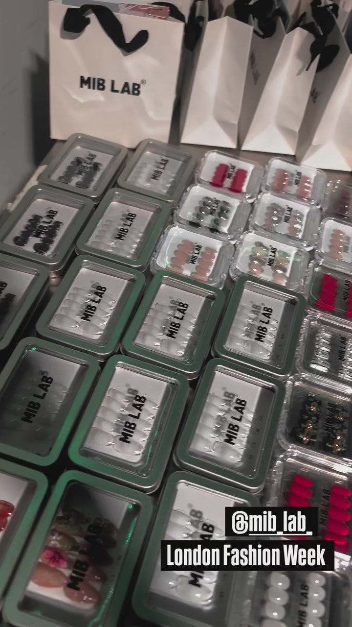 Coulisses London Fashion Week : table remplie de sets de press-on nails MIB LAB et sacs shopping MIB LAB, filmée en plan rapproché ; tag @mib_lab.