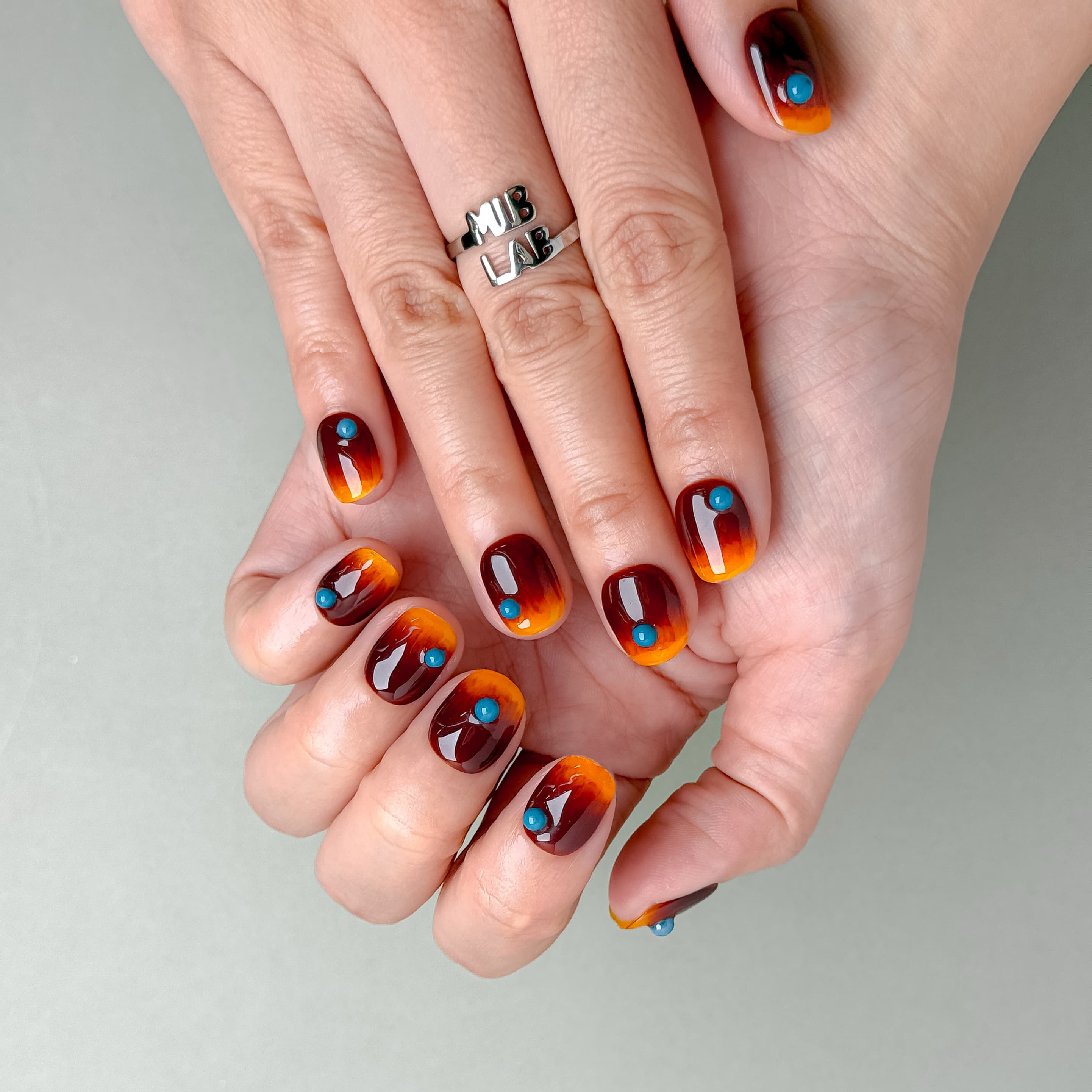 Détail How it’s Done sur mains : faux ongles premium réutilisables effet écaille, reflets ambrés, tenue longue durée, Suisse.