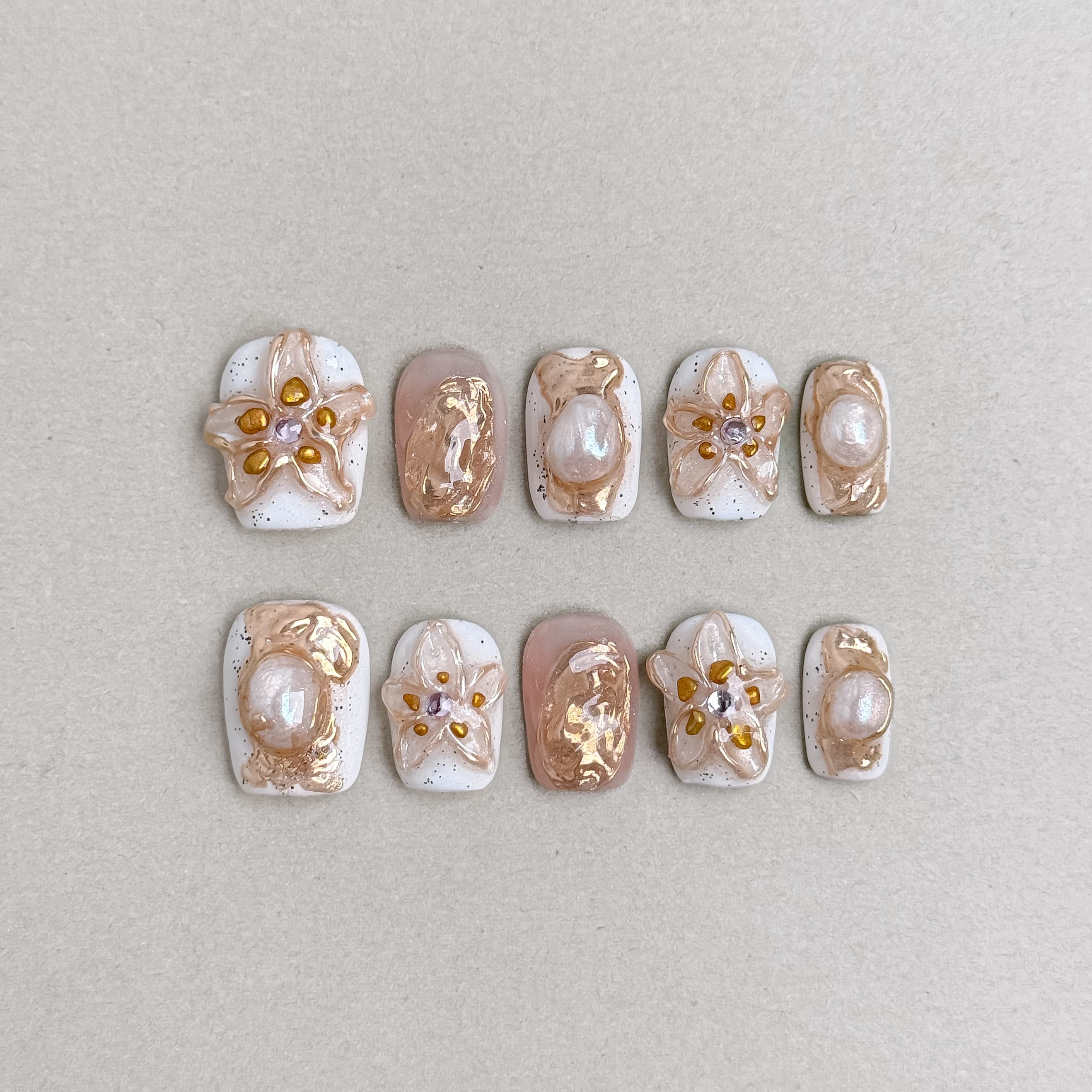 Stillness : faux ongles réutilisables nude laiteux, fleurs blanches et touches dorées, press on nails premium, finition brillante.