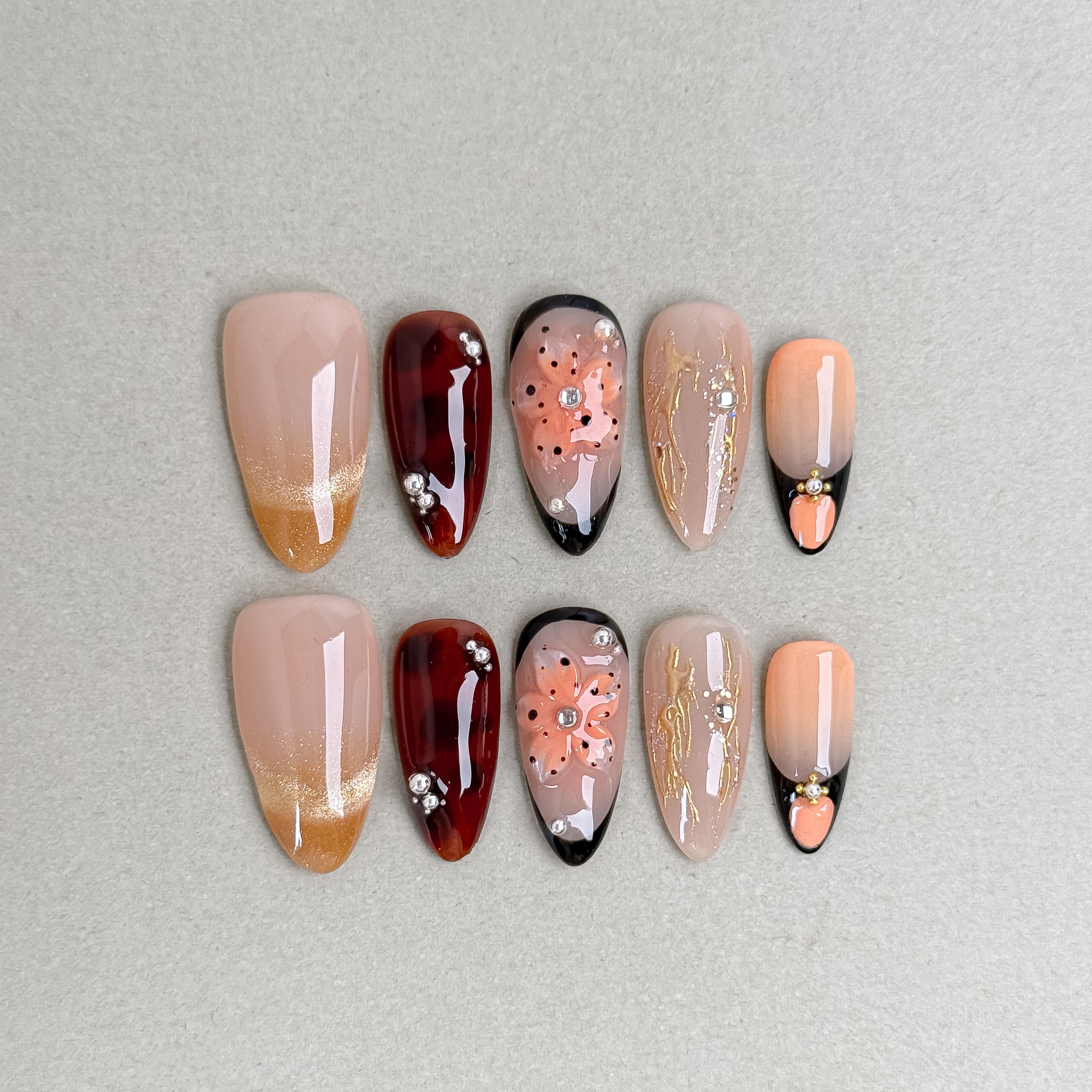 Maple-themed press-on nails with nude, gold, and red leaf designs arranged on a flat background