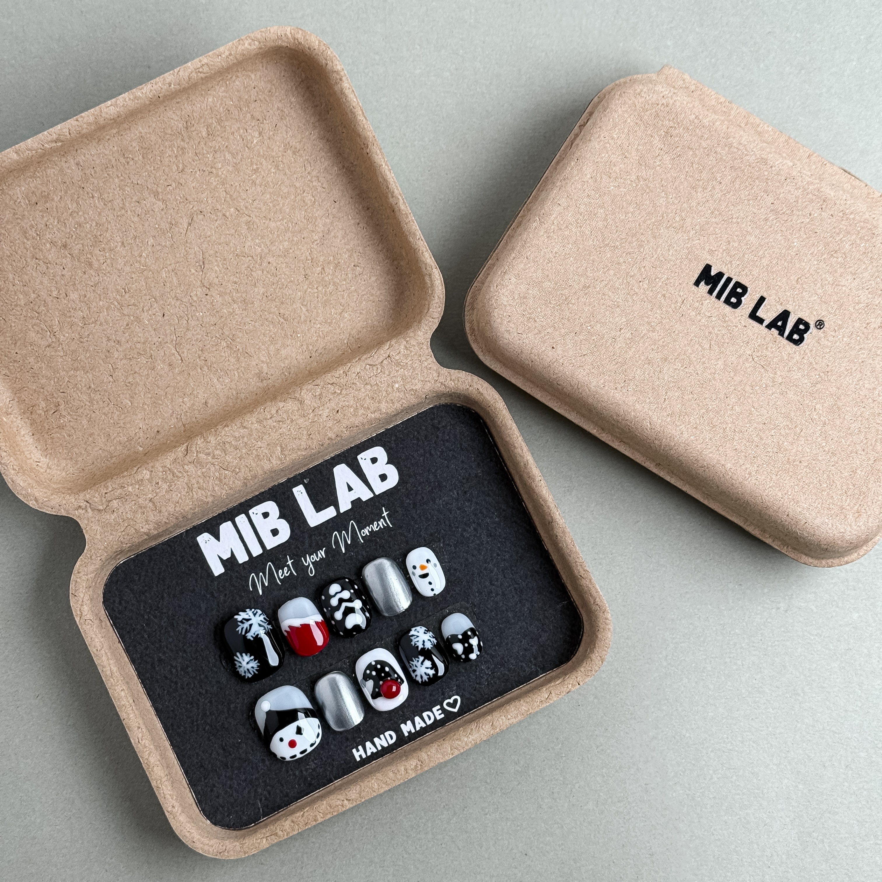 MIBLAB Inkmas press-on nail set featuring festive winter motifs in black and silver tones, packaged for boutique display in Geneva.