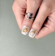 Gros plan Stillness : press on nails premium réutilisables fleurs blanches en relief, fini glossy, tenue longue durée, Suisse.