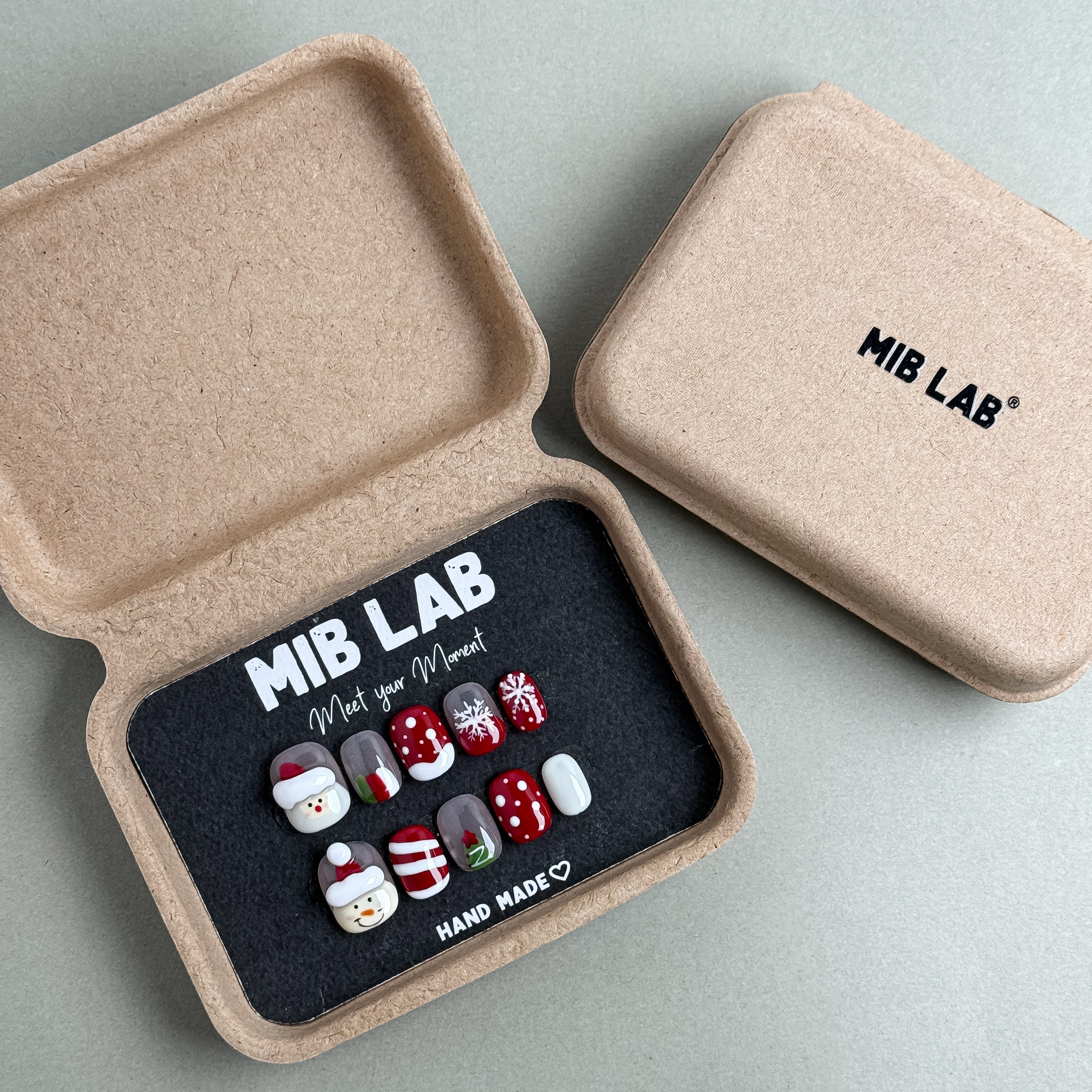 MIBLAB Santa Tell Me press-on nail set featuring festive Christmas motifs in red and white, packaged for boutique display in Geneva.