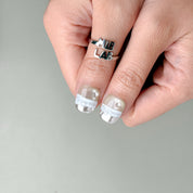 Deux mains avec The Light : press on nails premium lumineux, finition glossy, manucure rapide sans salon, Genève.